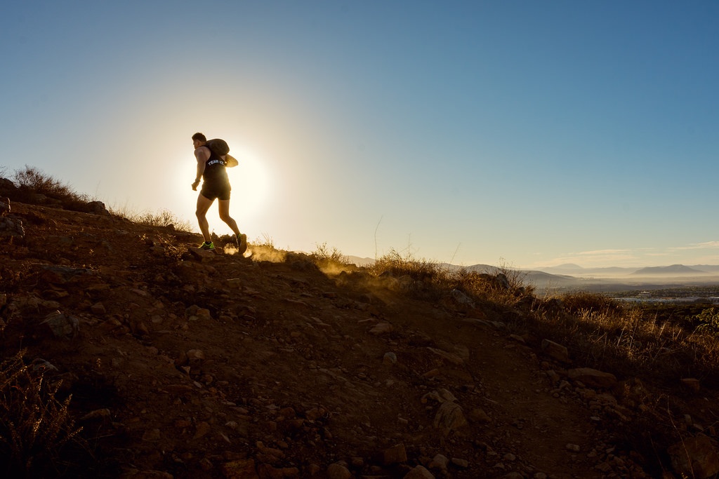 Image of a man running up a hill with a sandbag on his shoulders for his workout