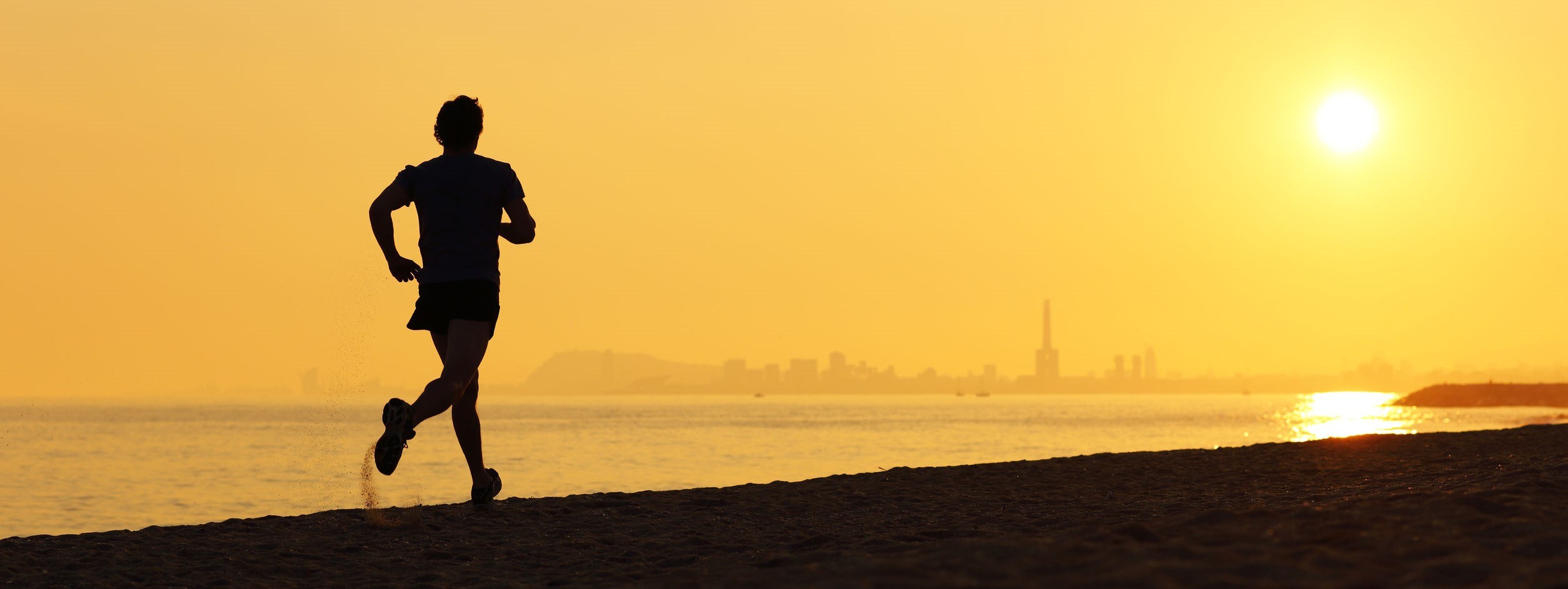 Jogger silhouette running on the beach at sunset with the horizon in the background