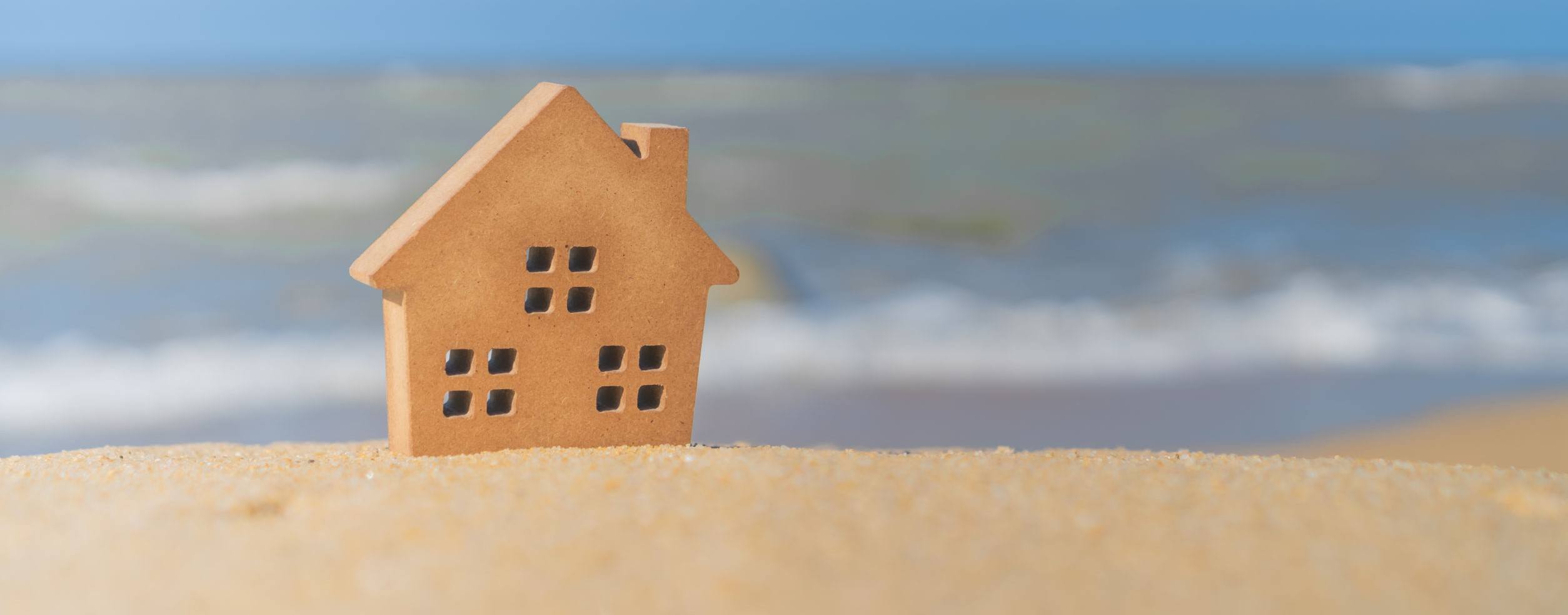 Closed up tiny home models on sand with sunlight and beach.