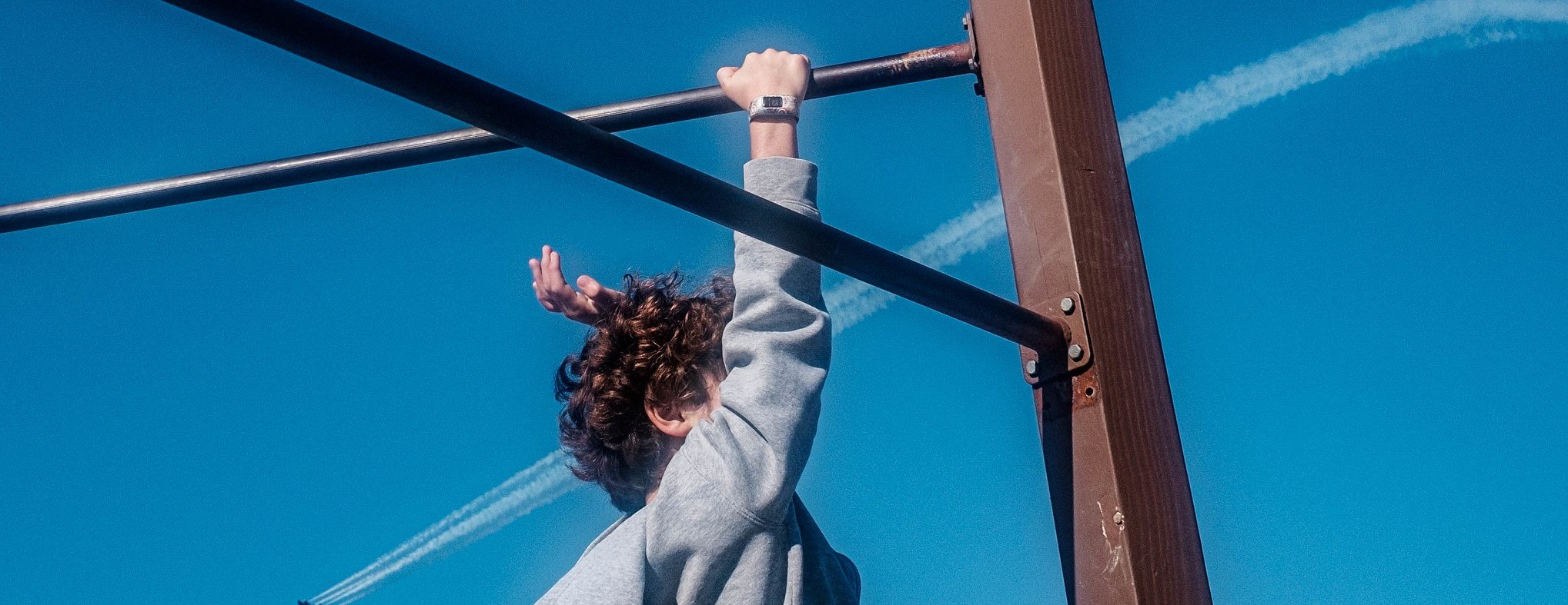 A kid holding himself up with one arm on a jungle gym.