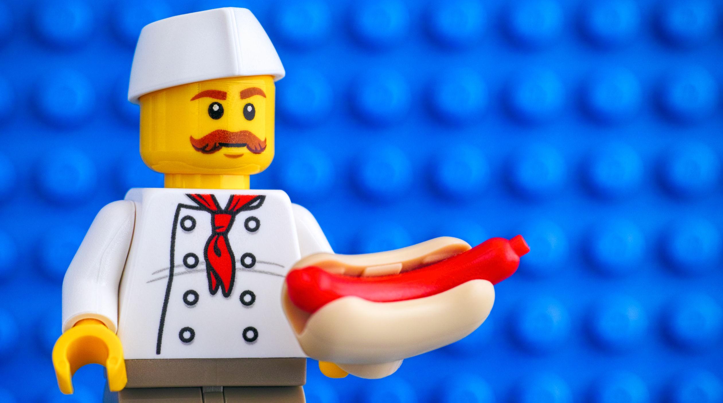 Lego chef with hot dog against blue baseplate backgrounds.