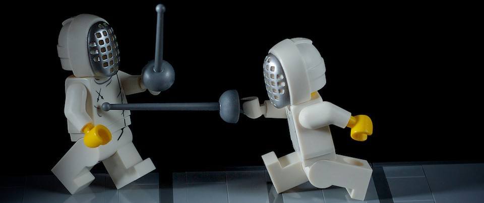A photo of one LEGO lunging at another with a sword.