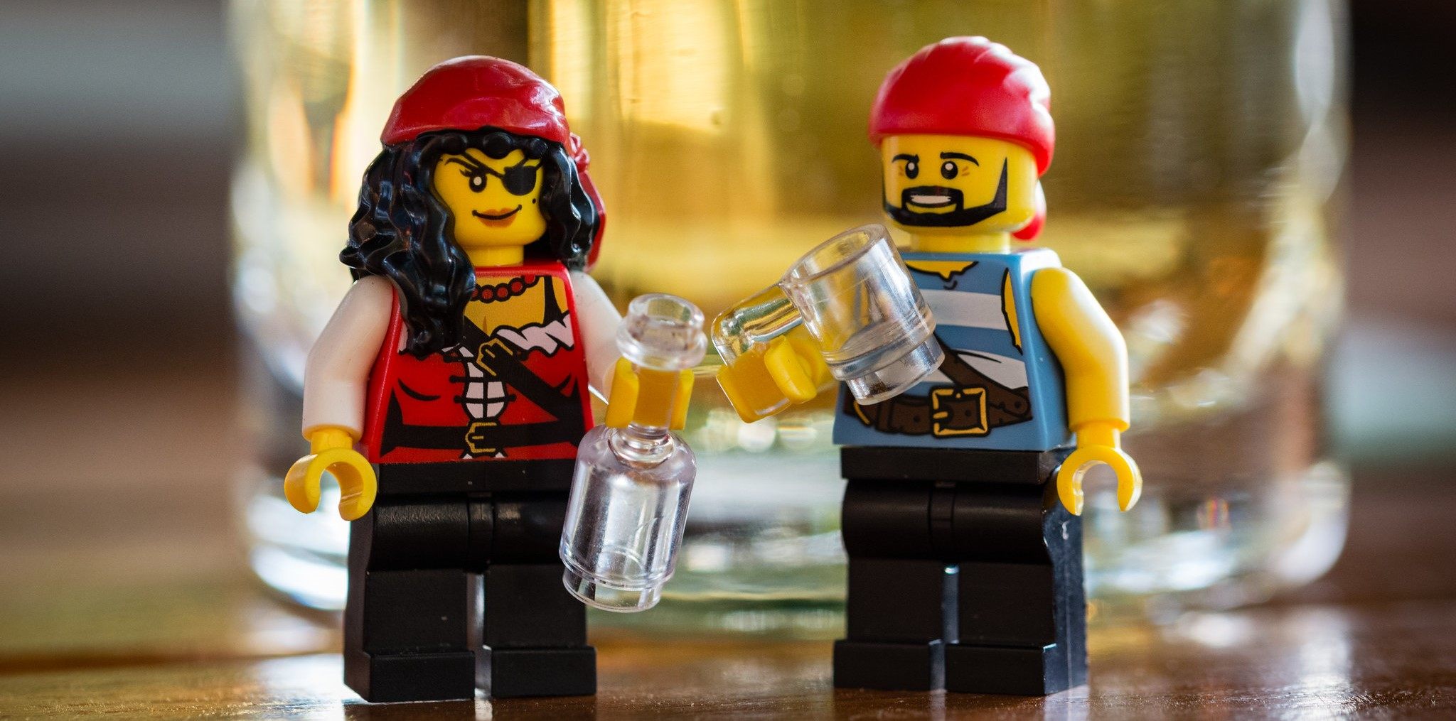 Two pirate LEGOS drinking in front of a glass.
